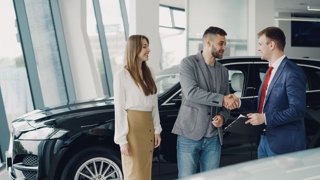 Home Customers shaking hands with dealer in showroom, sealing car purchase deal.