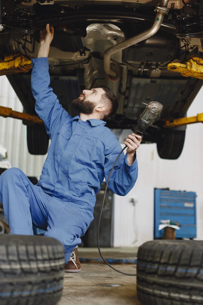 Home Mechanic in workwear inspecting vehicle underside in a garage environment. Service and maintenance concept.