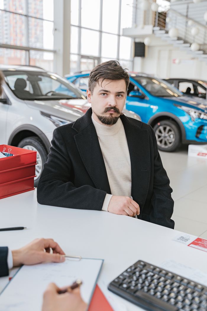 About A man in a coat discusses with a sales representative in a bright, modern car showroom.